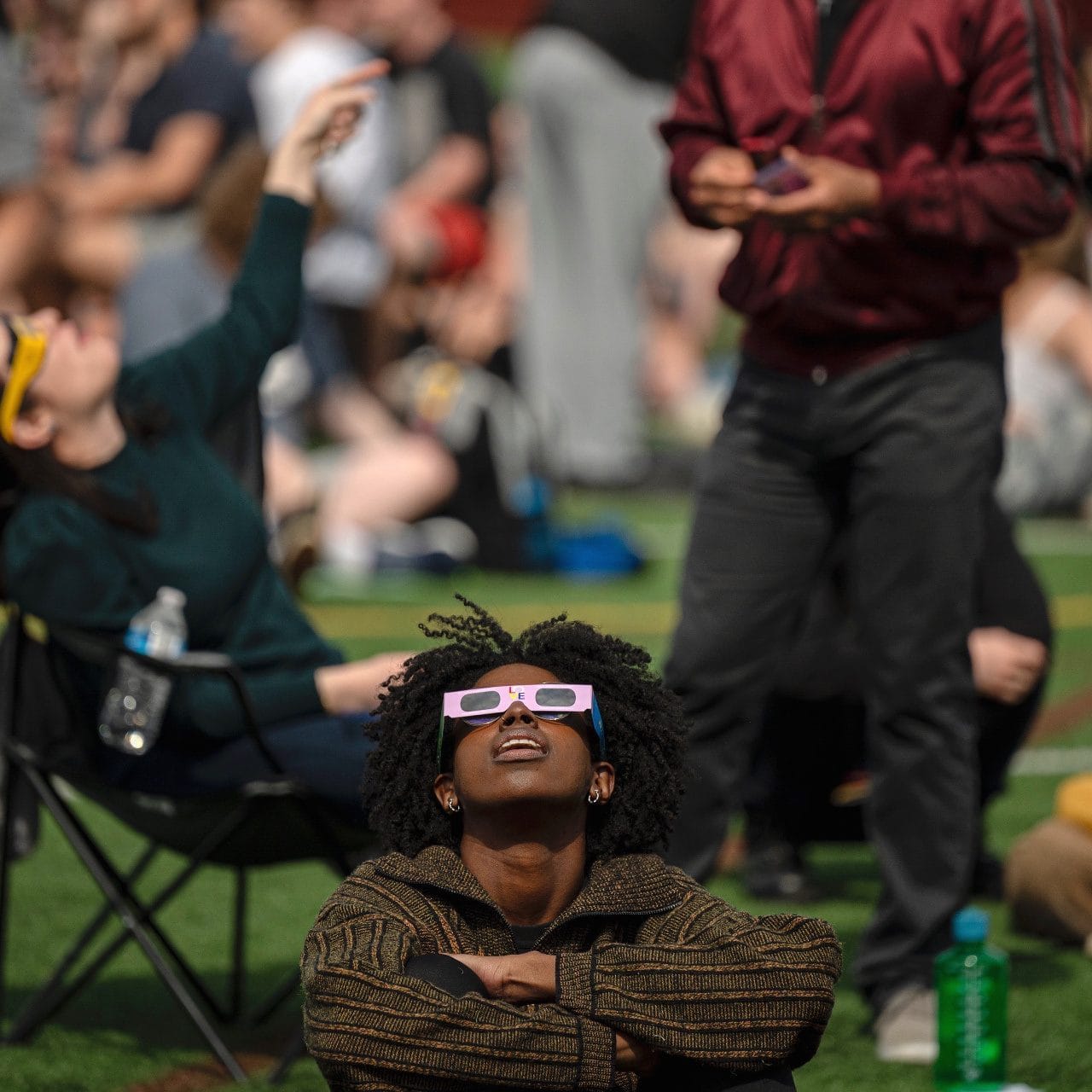People on a lawn in eclipse glasses looking up at the sky
