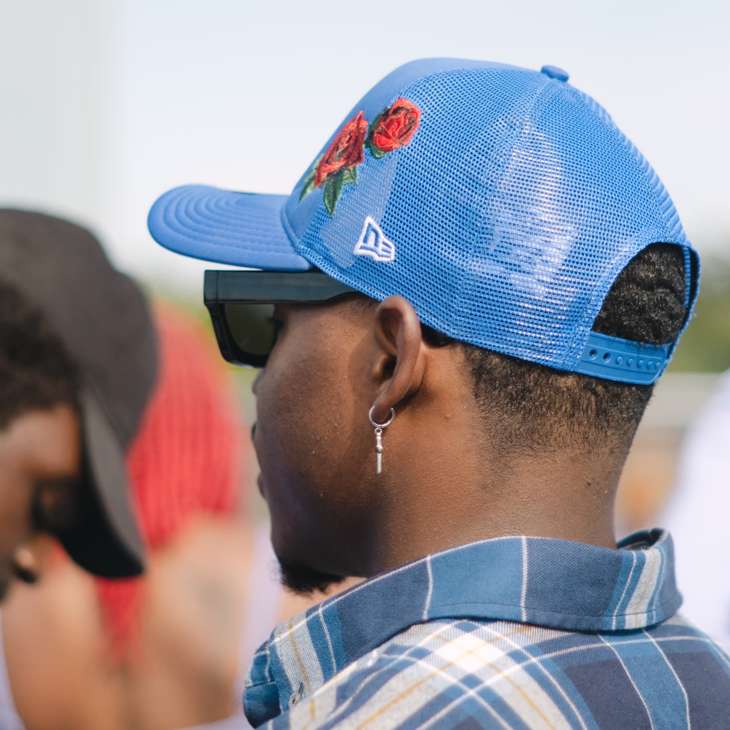 A person in sunglasses and a blue cap photographed from behind at an outdoor gathering