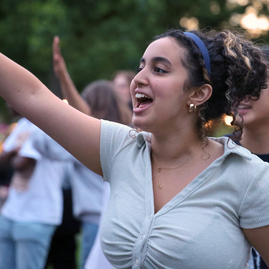 A student smiling and raising an arm during an outdoor gathering